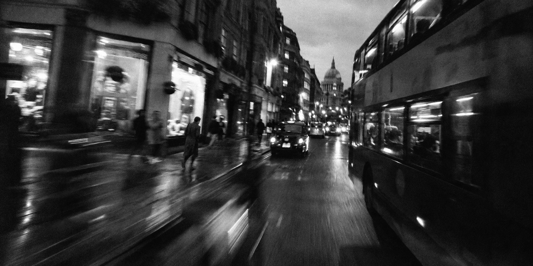 A London street at dusk shot from a moving vehicle, motion blurred